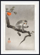 A framed Japanese-style art print depicting a gray monkey sitting on a dark branch with an orange persimmon and leaves, set against a light gray background with a white mat and black frame.