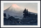 A framed Japanese-style art print depicting Mount Fuji with a pale pink peak, dark trees, stone buildings, and a stream in the foreground, shown with a white mat and black frame.