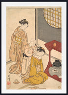 A framed Japanese ukiyo-e woodblock print depicting a woman in a beige kimono assisting a seated child in a yellow robe, with another child standing nearby, shown in a white mat and black frame.