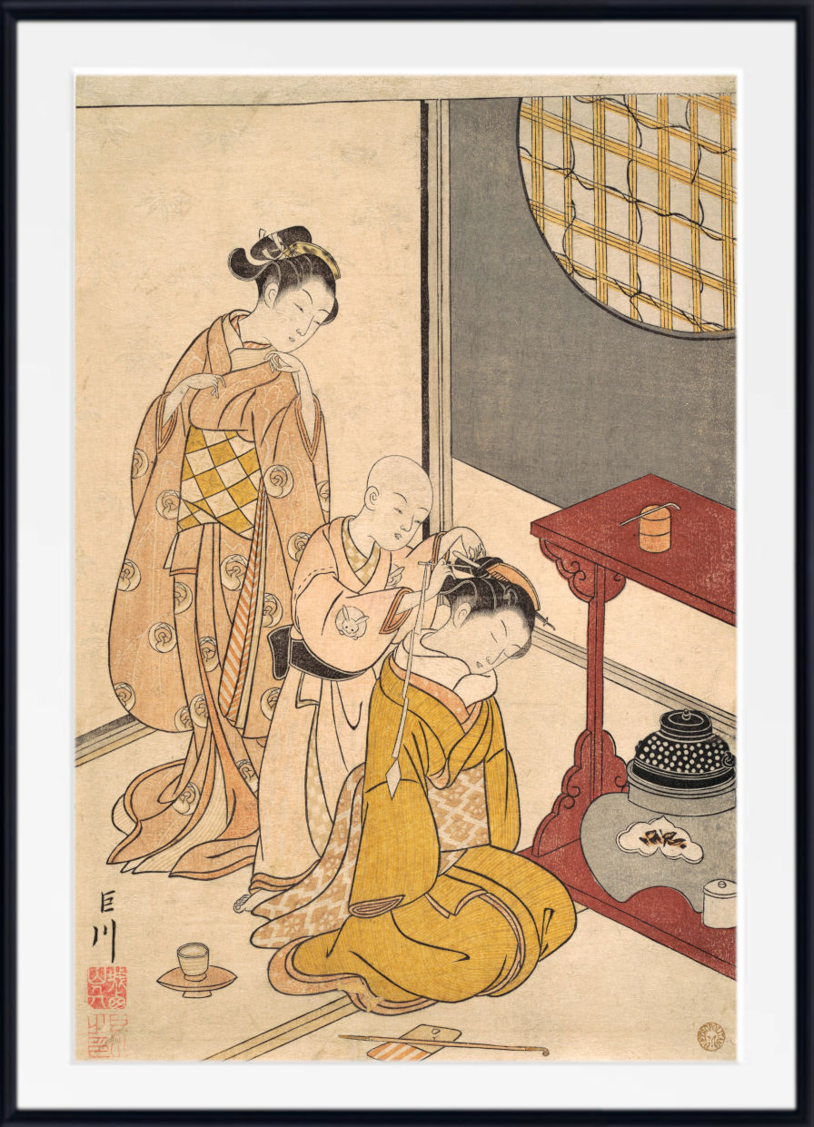 A framed Japanese ukiyo-e woodblock print depicting a woman in a beige kimono assisting a seated child in a yellow robe, with another child standing nearby, shown in a white mat and black frame.