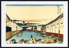 A framed Japanese ukiyo-e woodblock print depicting a canal scene with boats, buildings, mountains, and a pale sky, shown with a white mat and black frame.