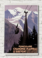 A vintage-style travel poster for a funicular railway in the French Alps, featuring snow-covered mountains, evergreen trees, and a cable car, displayed on a white brick wall.