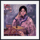 A framed painting of a woman in a pink patterned robe seated at a table with a vase of flowers, shown with a white mat and black frame.