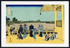 A framed Japanese ukiyo-e woodblock print showing figures in blue and black kimonos standing on a yellow boat deck, looking out over water toward Mount Fuji under a pale blue sky.