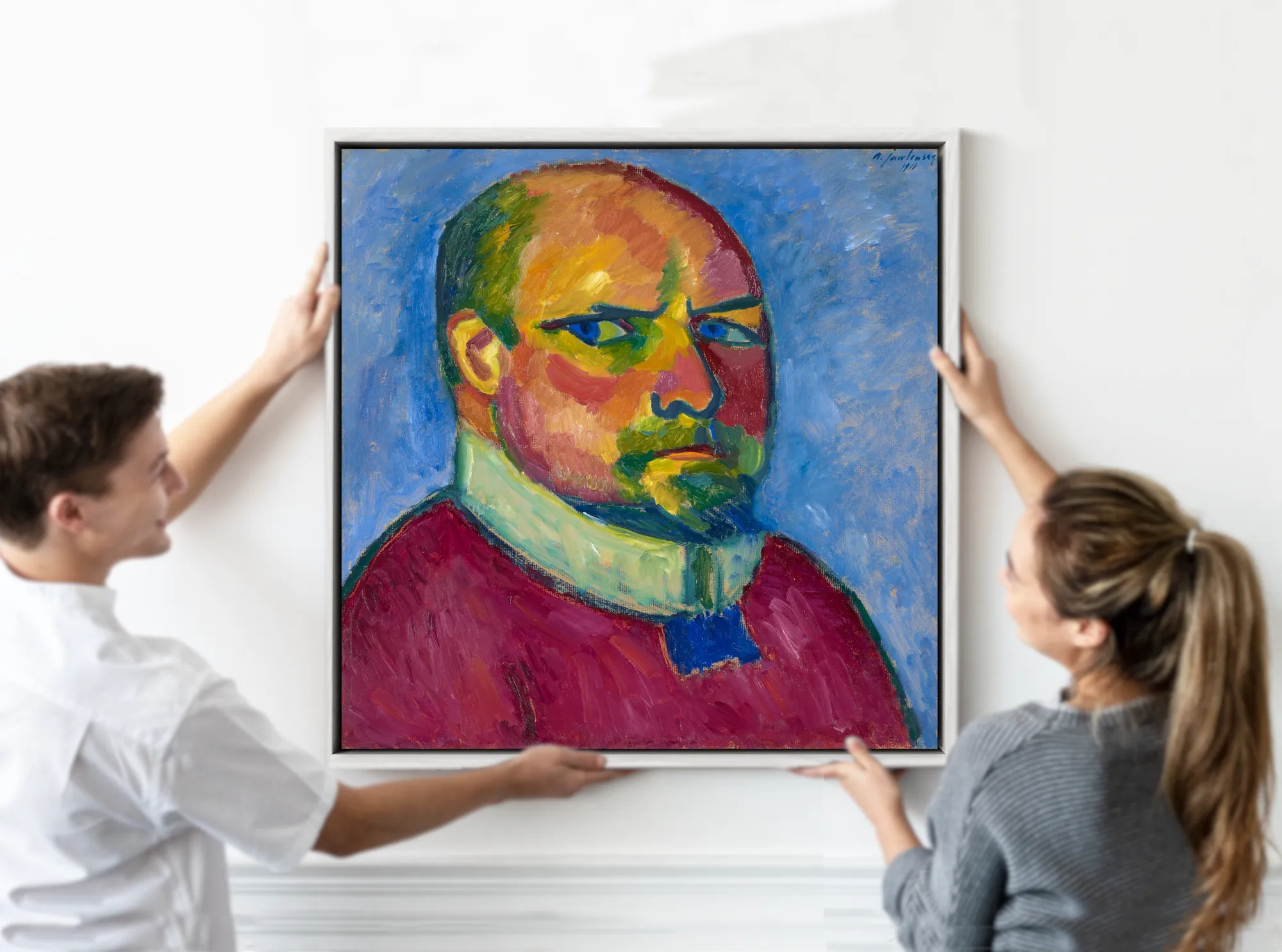 A framed portrait painting of a man with a bald head, green eyes, and a red coat is being held up by two people against a white wall.  Alexej von Jawlensky, Self Portrait (1911)