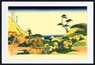 A framed Japanese-style landscape print with a wide white mat and black frame. The artwork shows rolling yellow-green hills, a lone tree, small figures, and a blue mountain or sea in the distance under a pale sky.