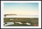A framed landscape painting depicting a calm body of water with distant hills, a small boat, and marshy foreground pools under a pale blue sky, shown with a white mat and black frame.