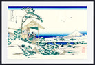 A framed Japanese-style art print depicting a snowy landscape with a small wooden pavilion, snow-covered trees, blue water, and a distant mountain under a deep blue sky.