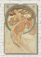 An Art Nouveau style poster print featuring a flowing female figure in warm peach, beige, and muted blue tones, displayed against a white brick wall background.