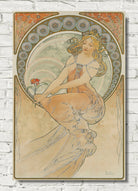 An Art Nouveau style poster print featuring a flowing female figure in warm beige, peach, and muted green tones, displayed against a white brick wall background.