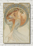 An Art Nouveau style poster print featuring a woman in flowing white drapery with a long orange-brown hair or scarf, framed by ornate gold and blue decorative borders. The print is displayed against a white brick wall background.