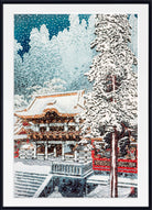 A framed art print depicting a snowy winter scene with a traditional Japanese temple, snow-covered trees, and falling snow, presented in a black frame with a white mat.