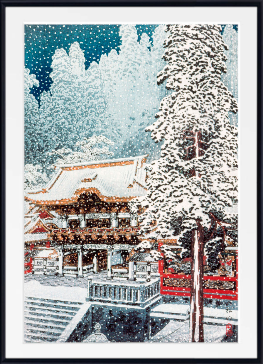 A framed art print depicting a snowy winter scene with a traditional Japanese temple, snow-covered trees, and falling snow, presented in a black frame with a white mat.