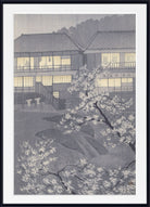 A framed Japanese-style art print depicting a traditional building with glowing windows and white flowering cherry blossoms in the foreground, shown against a dark background.