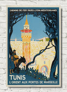 A vintage-style travel poster for Tunis, France, featuring a tower, trees, and a rider on horseback, displayed against a white brick wall background.