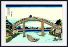 A framed Japanese-style art print depicting an arched wooden bridge over a calm blue river, with small boats, trees, and buildings. The print is shown with a wide white mat and a black frame.