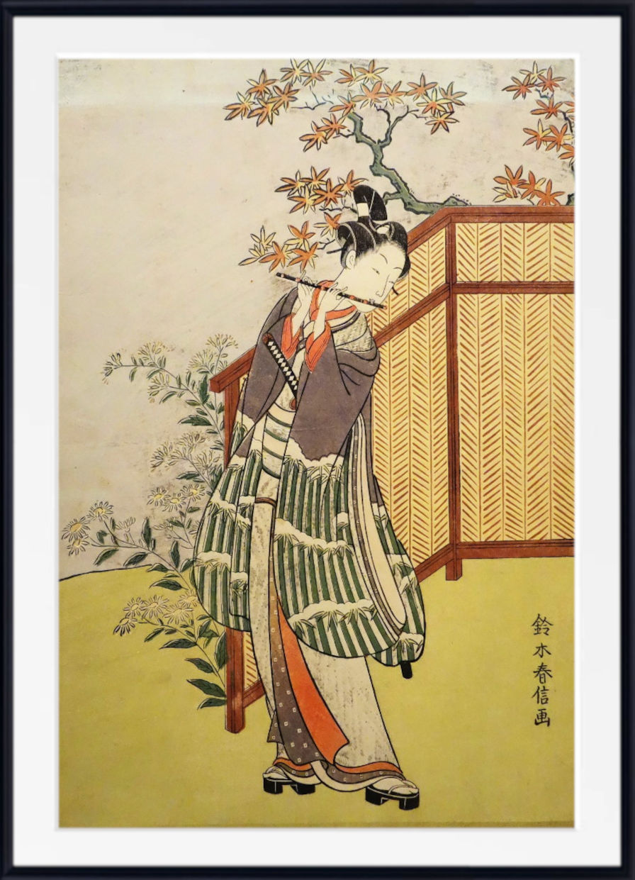 A framed Japanese ukiyo-e woodblock print depicting a woman in a striped kimono standing beside a folding screen with autumn leaves overhead, shown with a white mat and black frame.