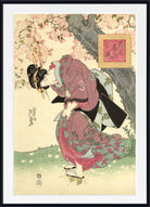 A framed Japanese ukiyo-e woodblock print featuring a woman in a flowing pink and green kimono beneath blooming cherry blossom trees, with a small framed artwork hanging on the wall. The print is shown with a white mat and black frame.