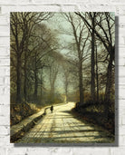 A vertical canvas print of a classical landscape painting depicting a path lined with tall, bare trees under a soft, hazy sky, with a small figure walking in the distance. The canvas is shown hanging on a white brick wall.