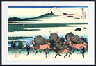 A framed Japanese woodblock-style art print showing a snowy mountain, water, and figures carrying large bundles of firewood on horseback. The print is mounted with a white mat and a black frame.