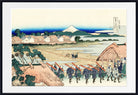 A framed Japanese-style art print depicting a coastal village scene with figures carrying long poles, thatched roofs, trees, water, and a snow-capped mountain in the distance.