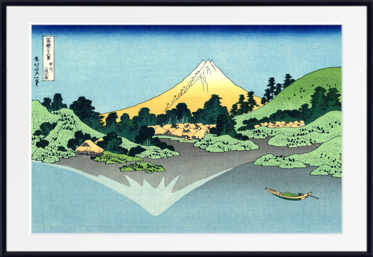 A framed Japanese-style landscape print showing Mount Fuji, green hills, trees, water, and a small boat, with a black frame and white mat.